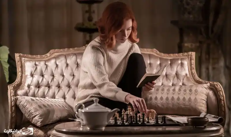 نمایی از مینیسریال The Queen's Gambit؛ زنی با کتاب در دست مقابل صفحه شطرنج.